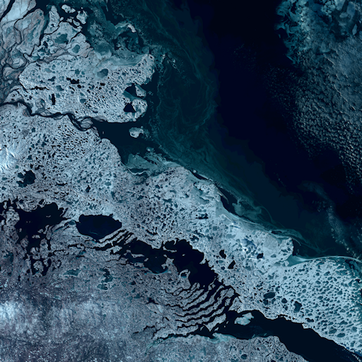 A satellite image of icy coastal tundra, jutting up against a dark blue ocean